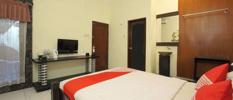 A hotel room with a bed, a TV, a small table with a kettle, a mirror, and a wardrobe.