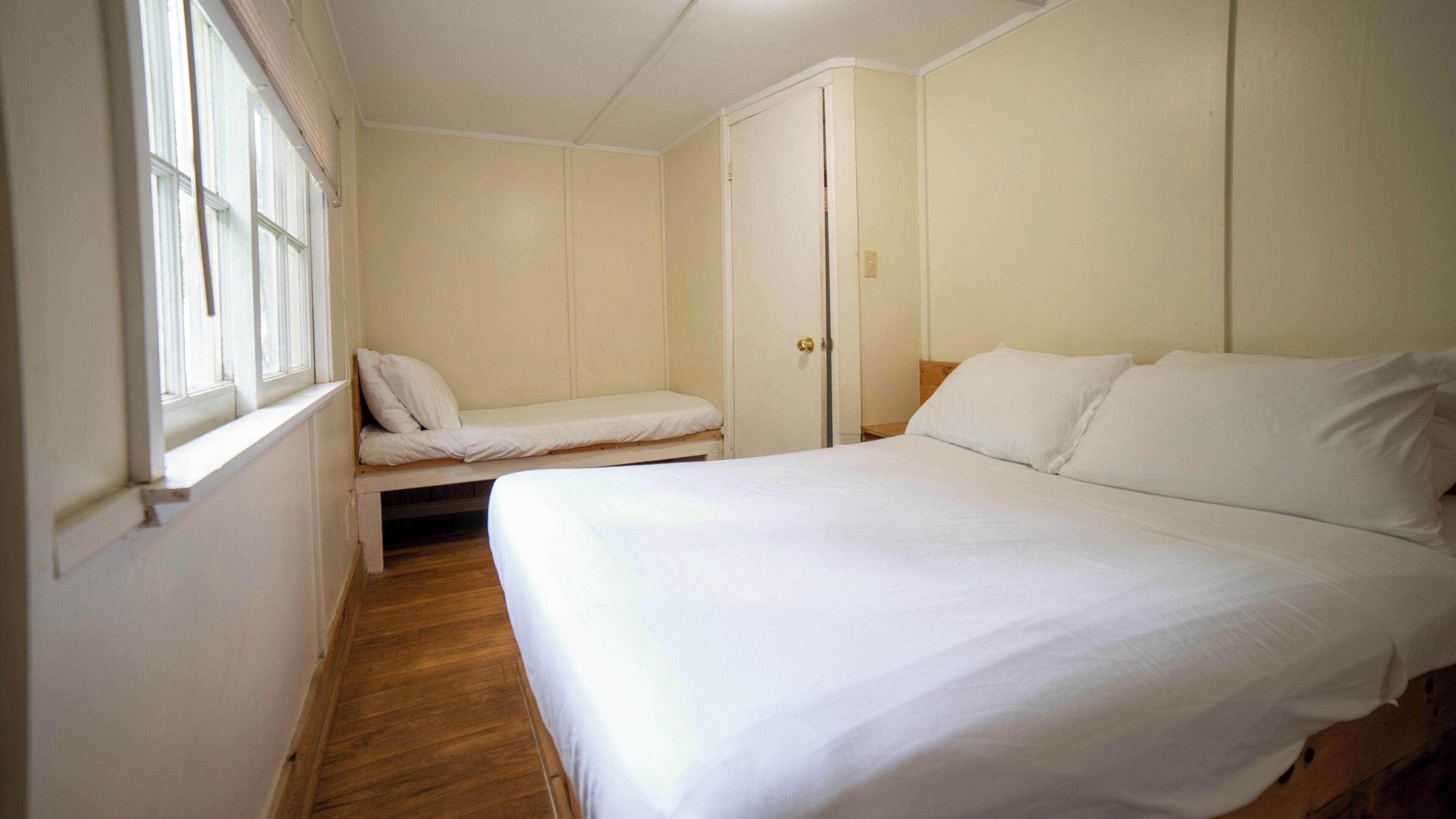 Une chambre avec un lit simple, un banc et une armoire.