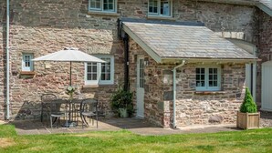 A stone building with a covered patio, a table with chairs, and a potted plant. - 1 Bed in Brecon (oc-42942) (Llanfrynach)