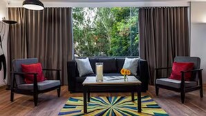 A room with a black sofa, two armchairs, a coffee table, a colorful rug, and a view of greenery through large windows. - Townhouse Midc Hadapsar (Pune)