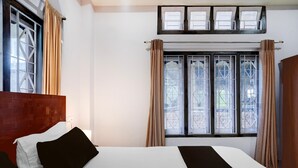 Habitación de hotel con una cama grande, cabecera de madera, ventana con cortinas y vistas a árboles.