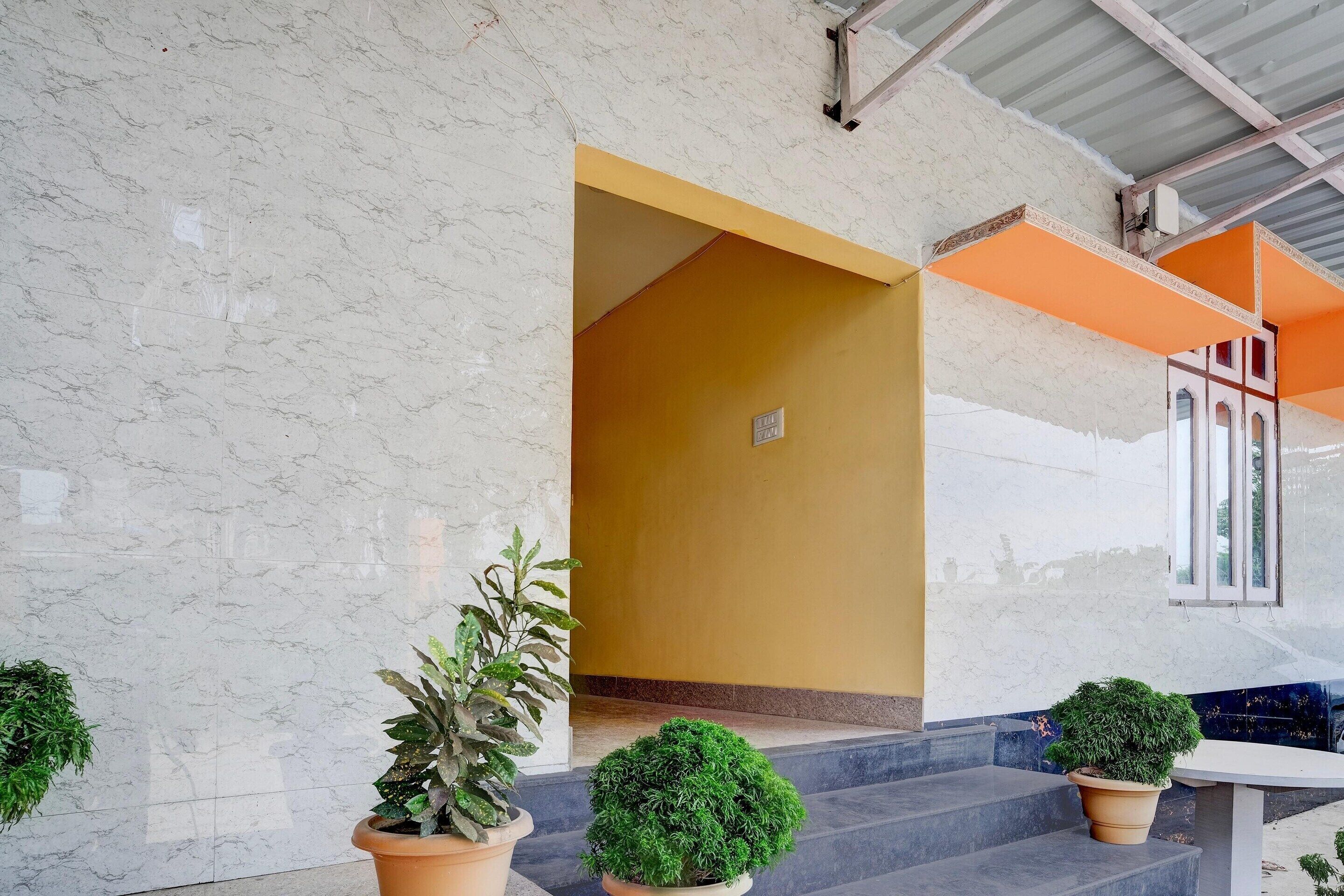 Entrada de un edificio con un muro de mármol, un marco de puerta amarillo y plantas en macetas.