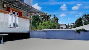 Una terraza en la azotea con un edificio blanco, una zona cubierta y follaje circundante.