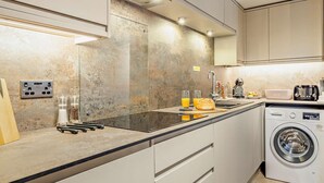 A modern kitchen with a built-in washing machine, a countertop with a toaster, and a glass cabinet with utensils. - 2 Bed in Barnstaple (oc-linor) (Hiscott)