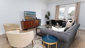 En stue med sofa, stole, et sofabord, et fjernsyn, et spiseområde og et stort vindue.