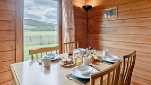 Eine Holzhütte mit gedecktem Esstisch für das Frühstück, Blick auf eine grüne Landschaft und Holzbalkendecke.