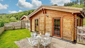 Eine Holzhütte mit Terrasse, Holzzaun und Rasenfläche.