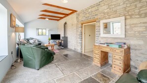 Amplia sala de estar con pared de piedra, chimenea, televisor y escritorio de madera.