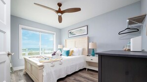 Un dormitorio con cama, mesitas de noche, ventilador de techo, ventana con vistas y cómoda.