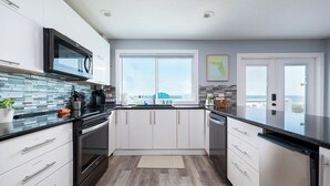 Una cocina moderna con armarios blancos, encimera negra, microondas integrado y un amplio ventanal con vistas.