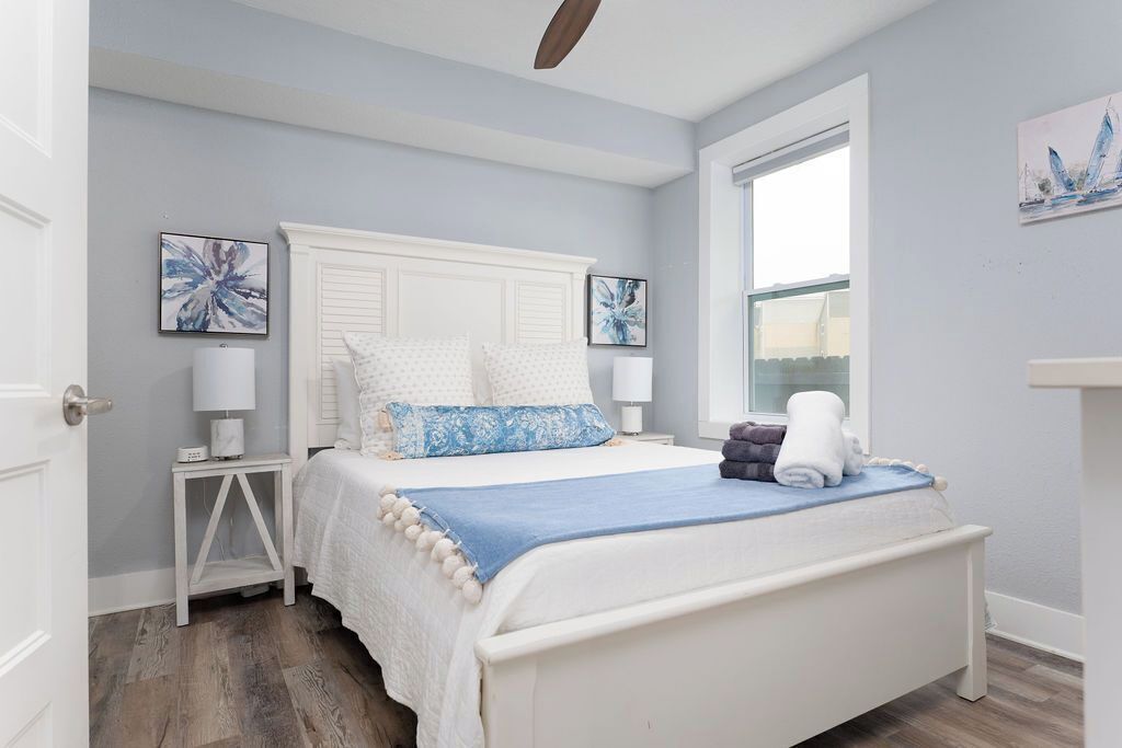 A bedroom with a white bed, a window, and artwork on the walls.