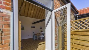 A room with a wooden floor, a dining table with chairs, and a brick wall. - 1 Bed in Barrow (oc-b42641) (Barrow)