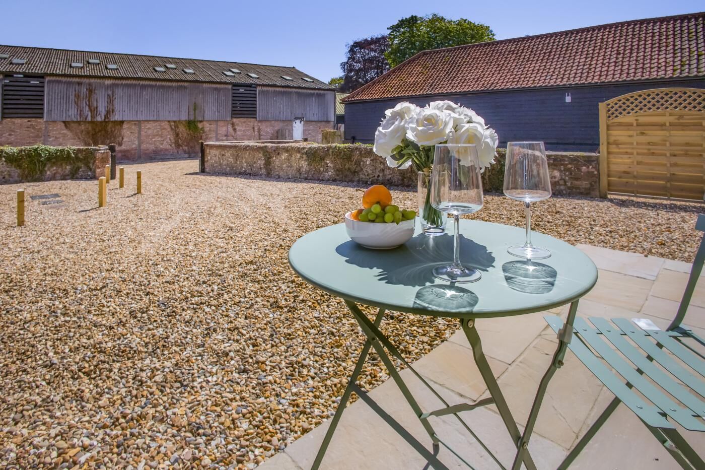 Une terrasse avec une table dressée pour deux personnes, un saladier rempli de fruits et un bouquet de fleurs.