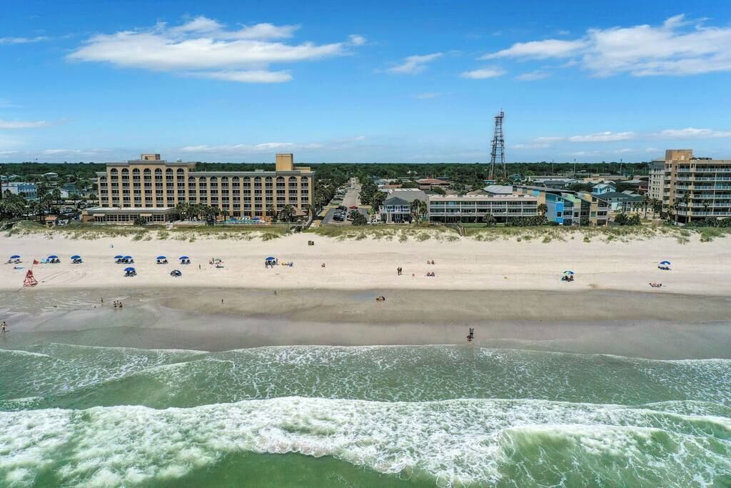 Un hotel frente a la playa con varias construcciones, una playa de arena y olas oceánicas.