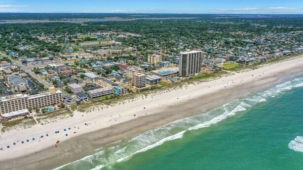 Vista aérea de una ciudad costera con una playa extensa, una zona residencial densa y un hotel destacado de varios pisos.