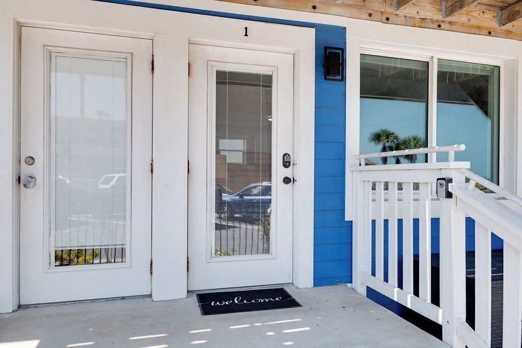 Una puerta blanca con un panel de vidrio, una pared azul y una barandilla blanca.