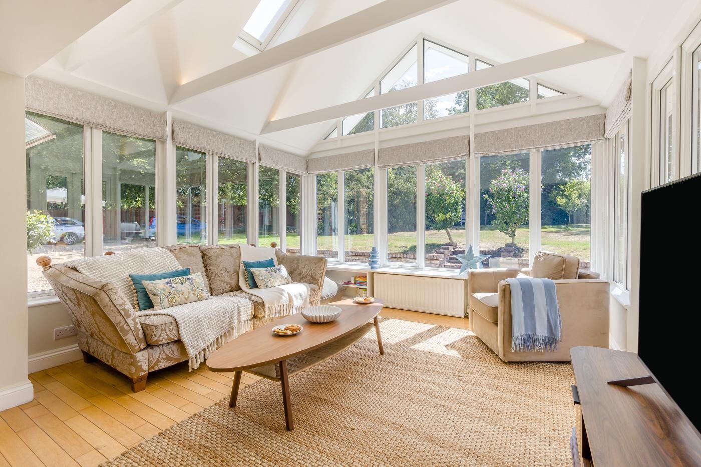 A spacious living room with a high ceiling, large windows, a sofa set, a coffee table, and a television.