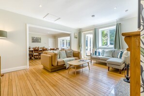 A spacious living room with a wooden floor, a beige sofa, a striped sofa, and a dining area with wooden chairs and a table. - 3 Bed in Northrepps (oc-f36625) (Overstrand)