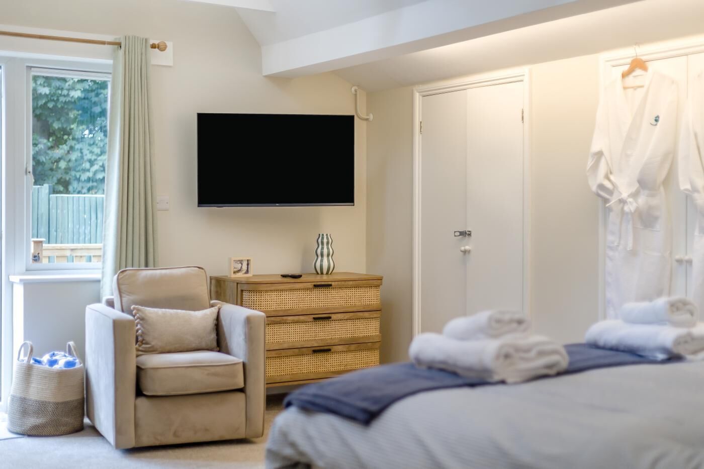 Quarto com cama, cadeira, televisão, guarda-roupa e janela com cortinas.