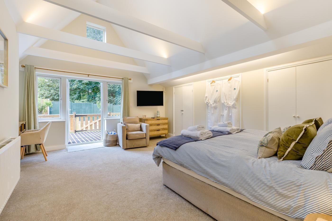 A bedroom with a large bed, a TV, a desk, and a chair. There is a sliding door leading to a balcony.