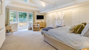 Une chambre avec un grand lit, une télévision, un bureau et une chaise. Une porte coulissante donne accès à un balcon.