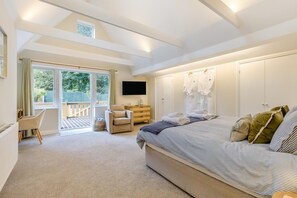Ein Schlafzimmer mit einem großen Bett, einem Fernseher, einem Schreibtisch und einem Sessel. Eine Schiebetür führt zu einem Balkon.