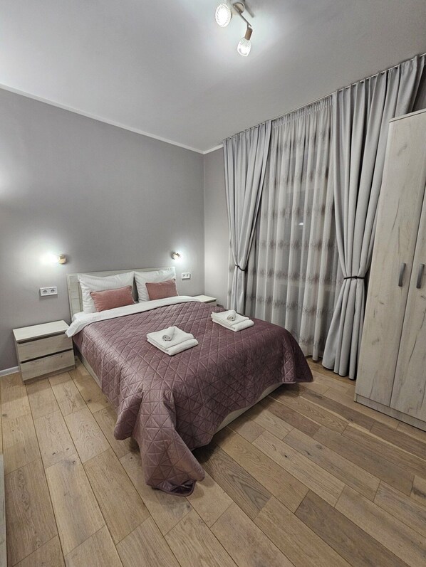 A bedroom with a bed, nightstands, a wardrobe, and curtains.