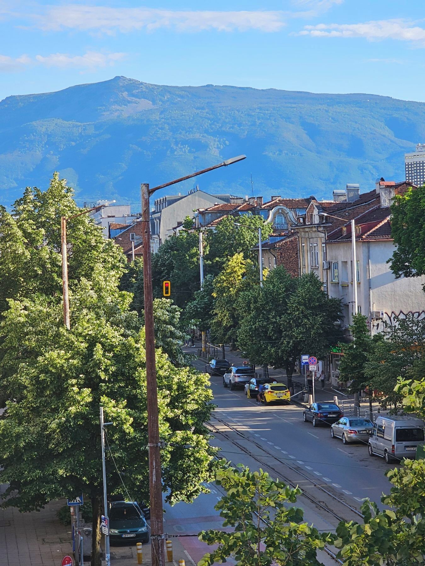 A street with buildings, a tram line, and a mountain in the background.