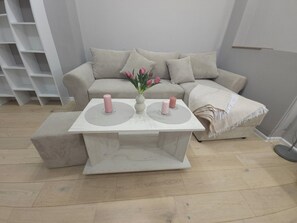 A living room with a beige sofa, a white coffee table with two pink candles, and a vase with pink flowers. - Metropolitan Stay 89 Apart City Center (Sofia)