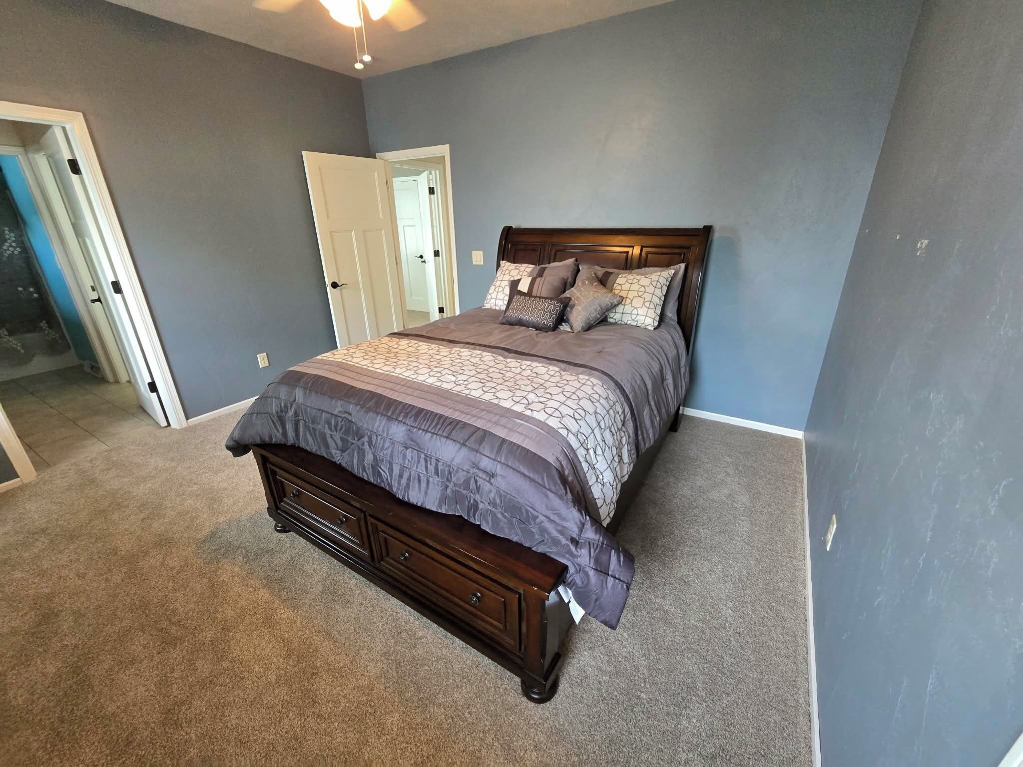 A bedroom with a bed, dresser, and a door leading to another room.