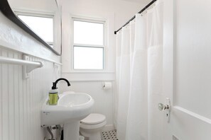 Ein kleines Badezimmer mit einem weißen Waschbecken, einer Toilette und einem Fenster oberhalb der Toilette.
