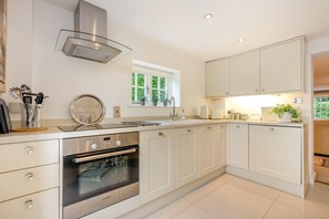 A modern kitchen with white cabinetry, a Bosch oven, a stainless steel range hood, and a window with a view of greenery.