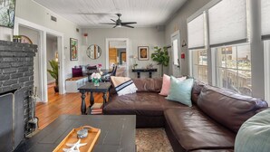 A spacious living room with a brown leather sectional sofa, a dining table with chairs, a fireplace, and large windows. - Fig Tree Inn | steps to the beach (Jacksonville Beach)