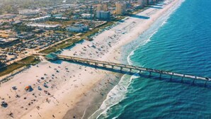 An aerial view of a beach with a pier extending into the ocean, surrounded by buildings and a sandy shoreline. - Fig Tree Inn | steps to the beach (Jacksonville Beach)
