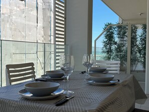 A dining table set with plates, bowls, and wine glasses, with a view of a building and trees through a glass partition. - Two-room apartment facing the sea with a view and a private parking space (Alba Adriatica)