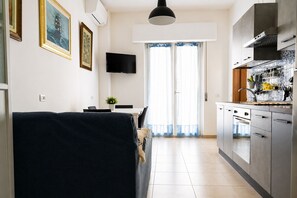 A modern kitchen with stainless steel appliances, a dining area with a TV, and a large window with curtains. - Two-room apartment facing the sea with a view and a private parking space (Alba Adriatica)