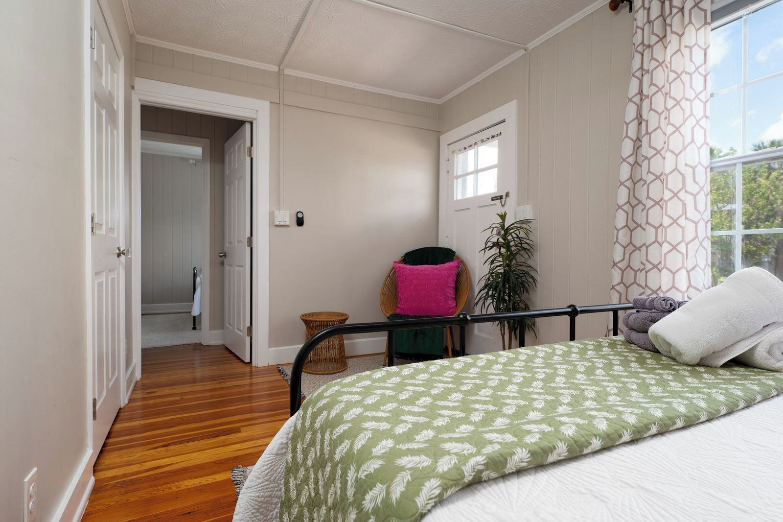 A bedroom with a bed, a window with curtains, a door, and a hallway.
