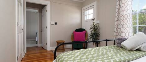A bedroom with a bed, a window with curtains, a door, and a hallway.