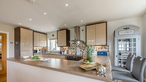 Une cuisine moderne dotée d’un grand îlot central, d’une cuisinière encastrée et d’un four à micro-ondes. Un panneau est accroché au mur, et il y a un meuble pour téléphone.