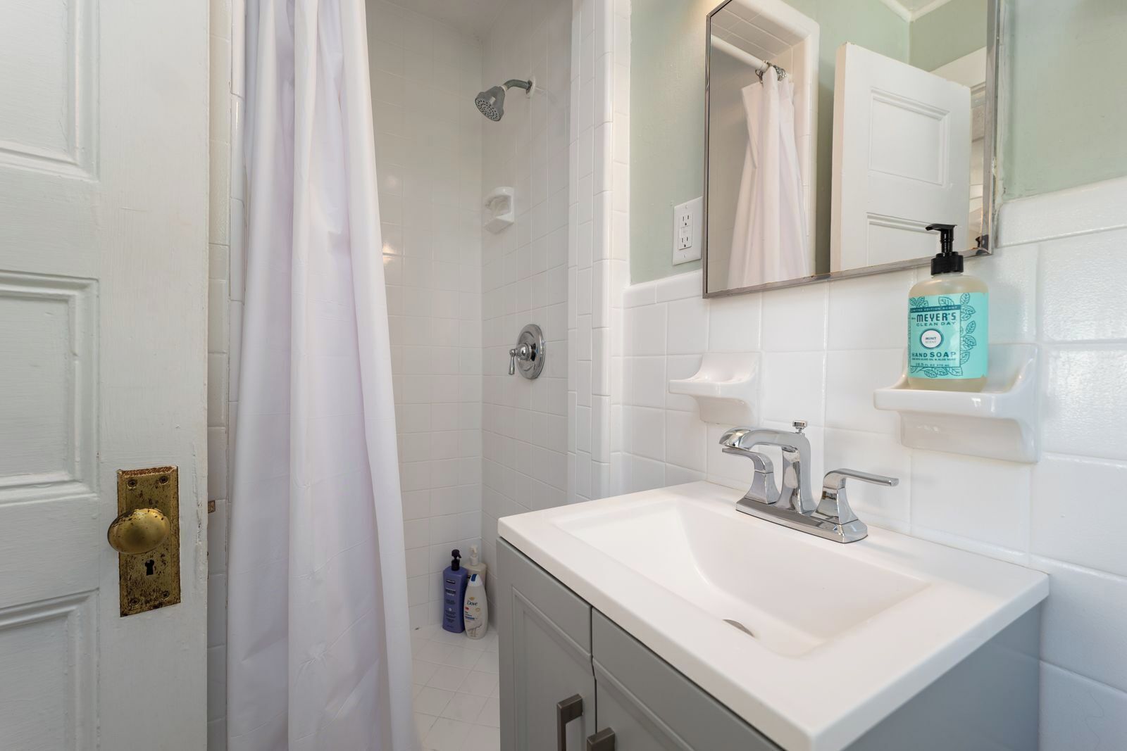 A bathroom with a shower, a sink, a mirror, and a bottle of soap.