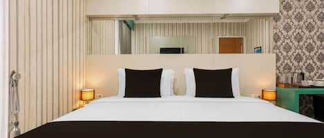 A hotel room with a large bed, two bedside lamps, a mirror above the bed, and a small table with a lamp.