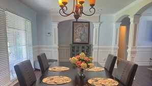 Comedor con una mesa de madera oscura, seis sillas, una araña y un florero.
