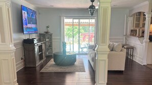 Amplia sala de estar con pisos de madera, un televisor de pantalla plana grande, una zona de estar acogedora con sofá y una mesa de centro redonda, y una puerta corrediza de vidrio que da a un patio al aire libre.