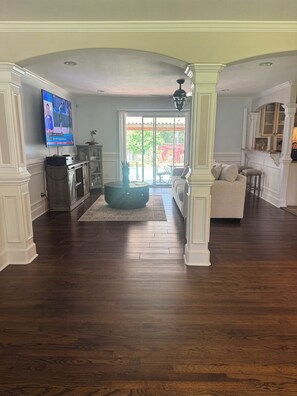 A spacious living room with hardwood floors, a large flat-screen TV, a cozy seating area with a sofa and a round coffee table, and a sliding glass door leading to an outdoor patio. - 3-bedroom house in serene Warner Robins with cool AC and a pool. (Warner Robins)