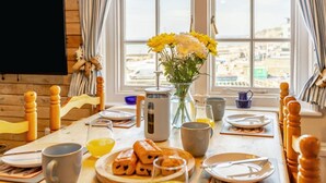 Ein Esstisch mit Frühstücksgebäck, eine Vase mit Blumen und Blick durch das Fenster.