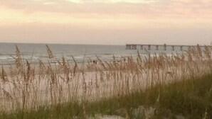 A beach with tall grasses in the foreground and a pier extending into the water. - Vacay or Relocation Home | 3 min walk to beach (Neptune Beach)