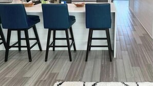A modern kitchen with white cabinets, a stainless steel refrigerator, and a bar area with blue chairs. - Vacay or Relocation Home | 3 min walk to beach (Neptune Beach)