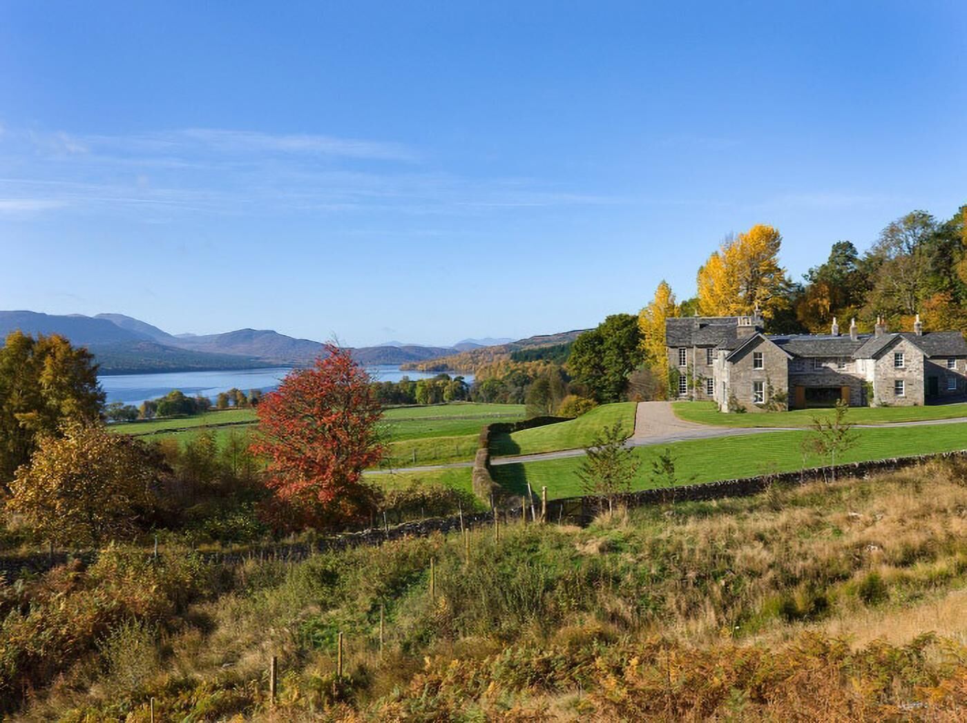 A stone building with a lawn and a lake in the background.