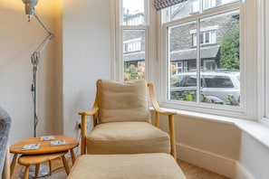 Ein Eckzimmer mit Holzstuhl, einem kleinen Tisch und einem Fenster mit Blick auf Gebäude und parkende Autos.