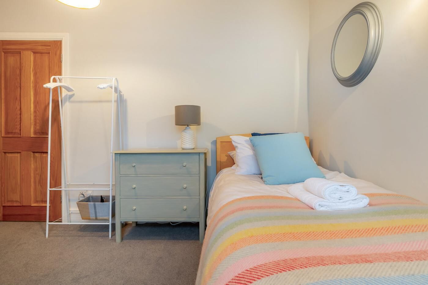 A bedroom with a bed, a nightstand, a dresser, a mirror, and a wardrobe.